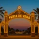 Illuminated entrance arch of the Feria de Vera 2025 with palm trees at twilight in Vera, Almeria