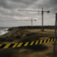 Coastal construction zone with cranes and warning tape near fragile cliffs, representing environmental risks linked to the Palomares PA-4 urbanisation project.