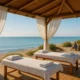 Massage therapy cabin by the sea with fluttering curtains and blue Mediterranean water.